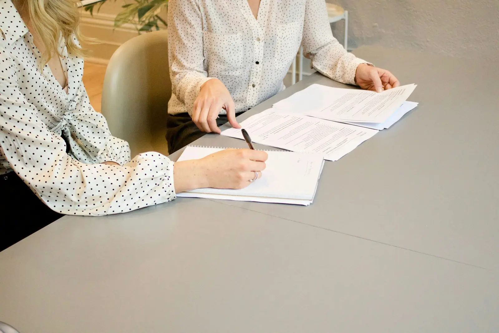 Zwei Personen am Tisch gehen Vertragsunterlagen durch, eine schreibt mit